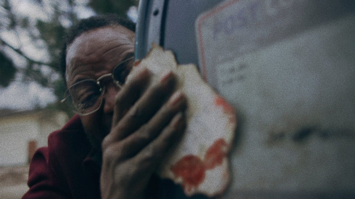 In Dead Mail, Sterling Macer Jr. holds a bloody letter next to a post box, wearing a strained expression on his face