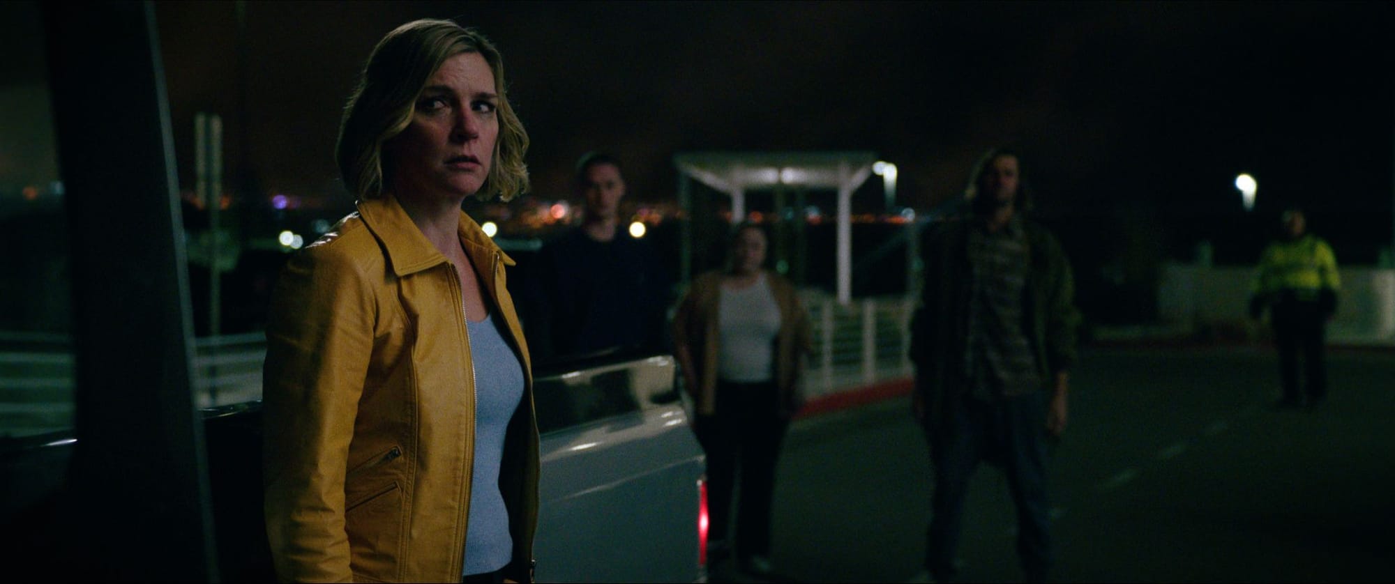 Rhea Seehorn looks suspiciously around her as people stand in the background in Pluribus