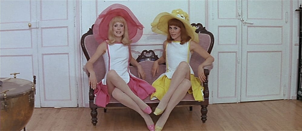 Catherine Denueve and Françoise Dorléac wearing bright pastel colors and sitting in a chair in The Young Girls of Rochefort