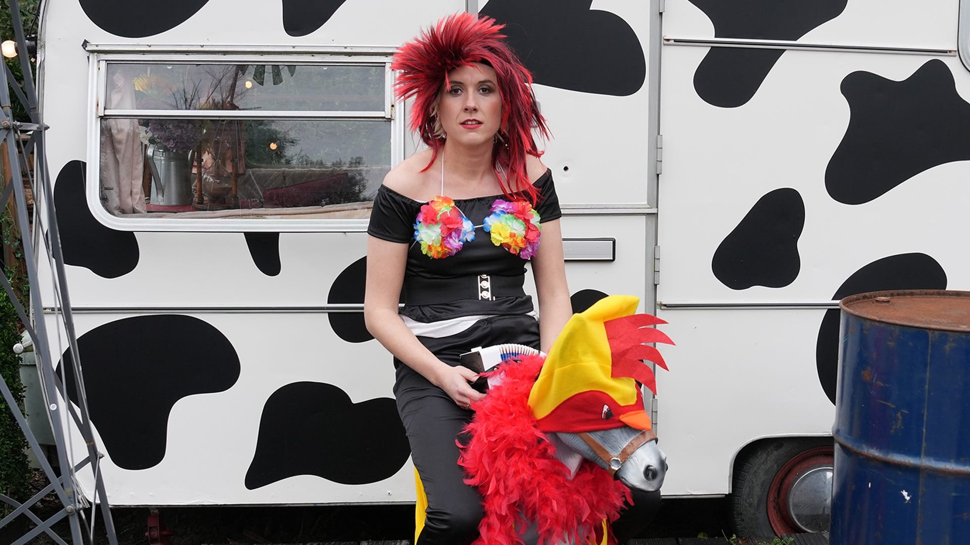 Maisie Adam sits on a toy donkey while wearing a silly wig and hula top