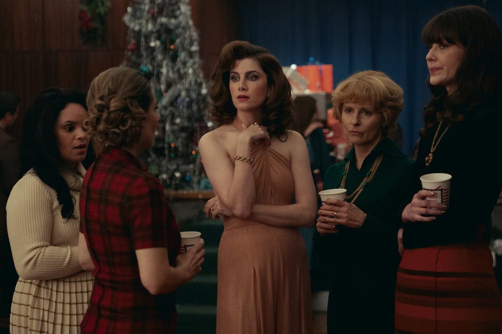 Vic Michaelis in a fancy dress with fancy hair, surrounded by co-stars in Ponies at a holiday party