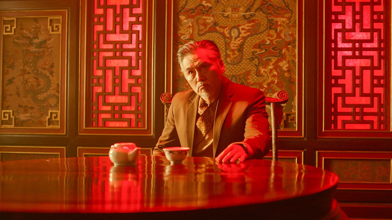 Chunyu Shanshan as Wang, sitting at a table in his restaurant in The Forbidden City