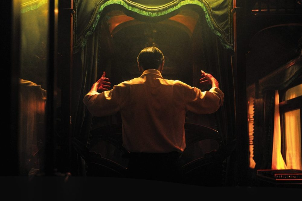 In Resurrection, a man holds his hands up like a conductor in front of a mirror