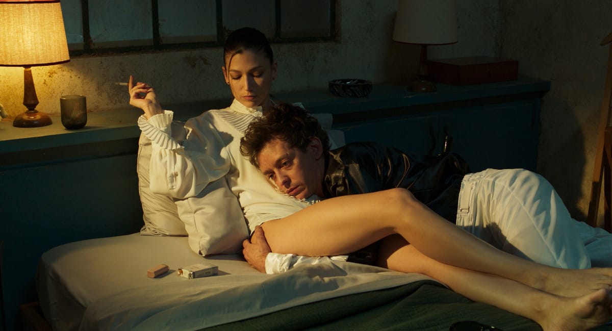 Nahuel Pérez Biscayart and Úrsula Corberó lie together on a bed in Kill the Jockey. Biscayart has a distanced look on his face, as Corberó smokes a cigarette