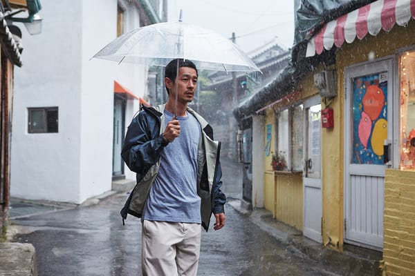 Ryo Kase walks under an umbrella in the rain in Hill of Freedom