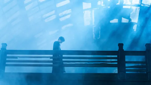 A man walks with his head down across a blue-lit bridge in Resurrection